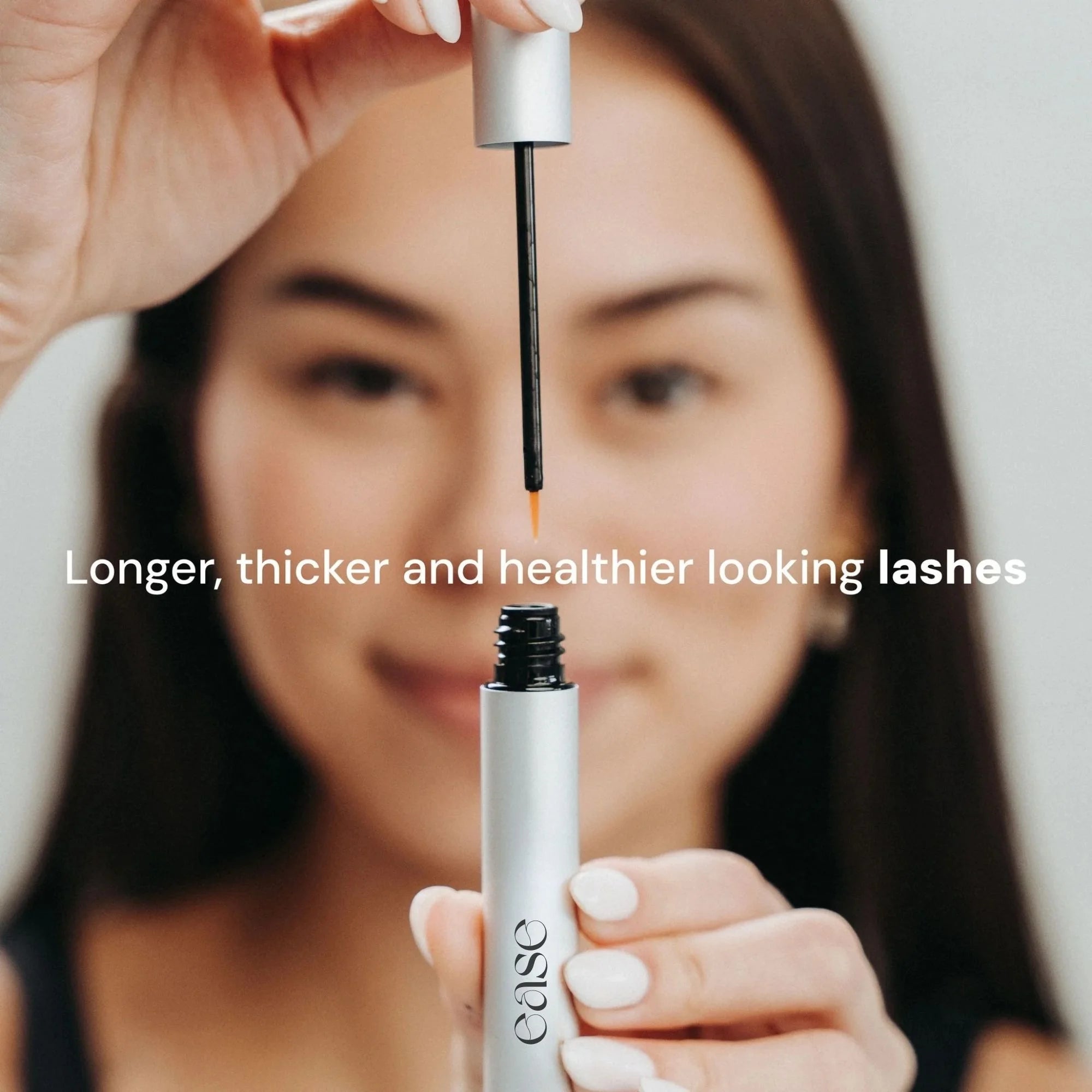Person holding a eyelash serum with text 'Longer, thicker and healthier looking lashes' against a neutral background.